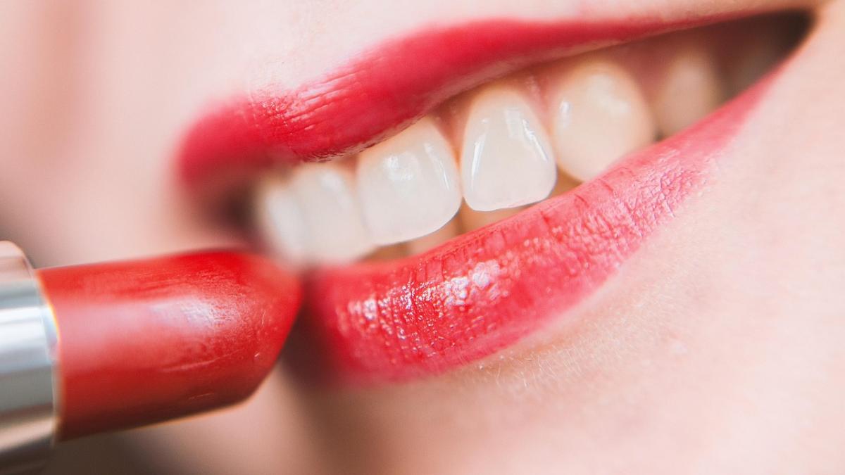 Крупный план губ: женщина наносит яркую красную помаду