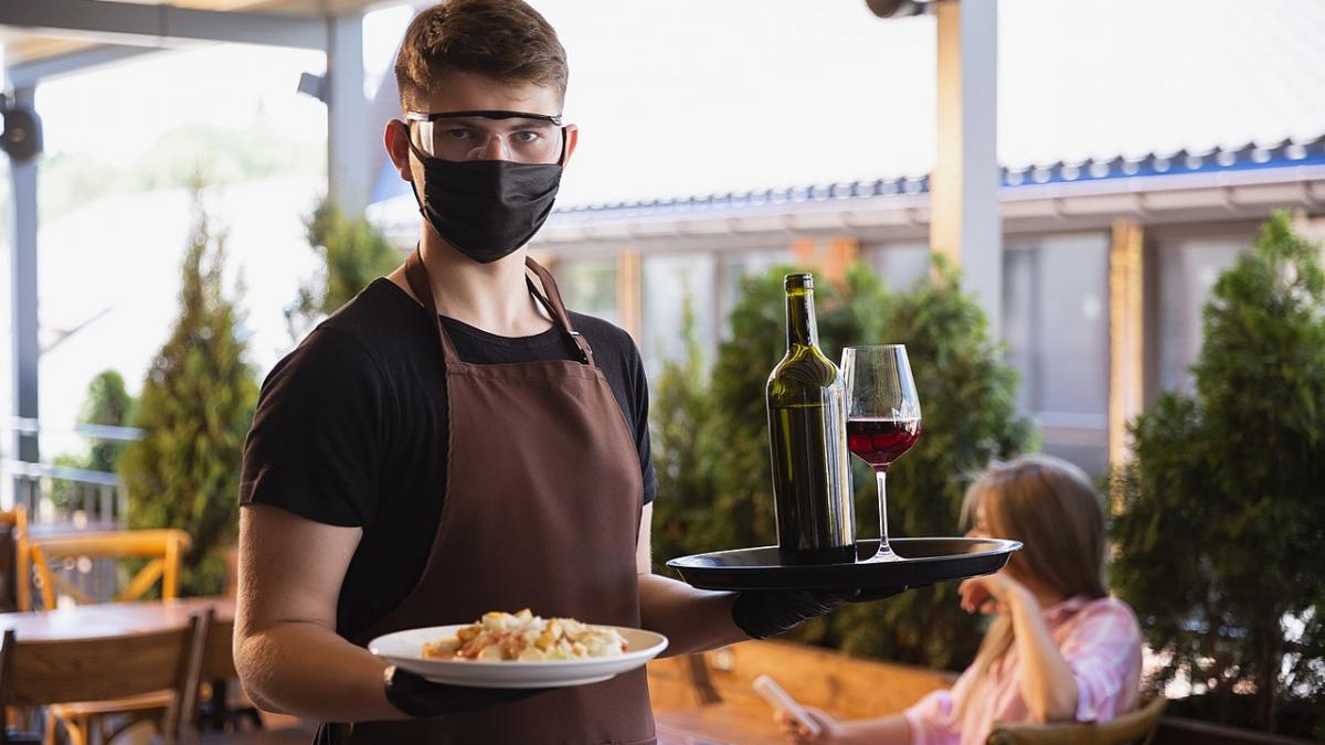 Официант работает в ресторане в медицинской маске и перчатках во время пандемии коронавируса
