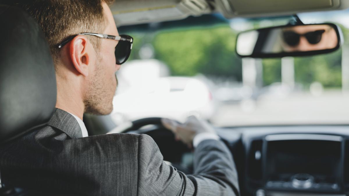 Мужчина в тёмных очках смотрит в зеркало заднего вида