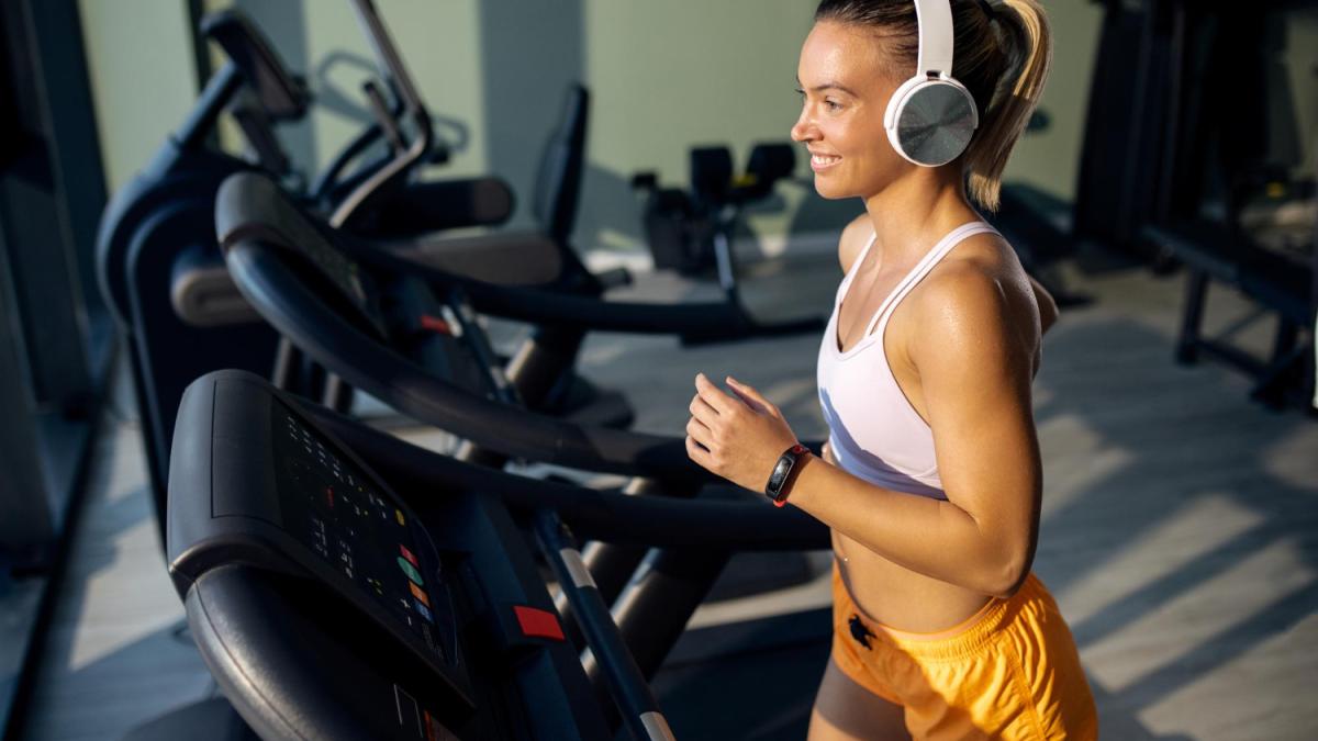 Девушка с наушниками бегает по беговой дорожке