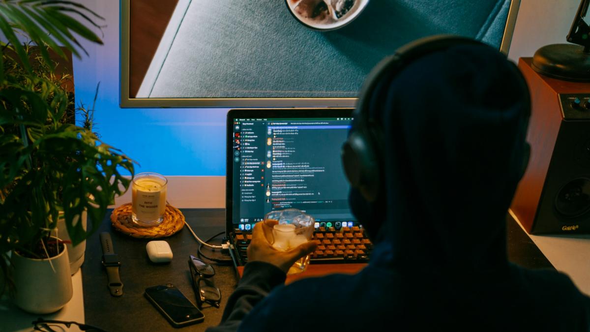 Хакер в капюшоне сидит перед монитором с кодом