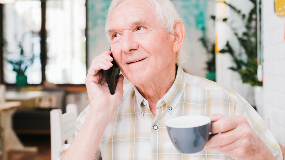 Пожилой мужчина с чашкой чая разговаривает по телефону