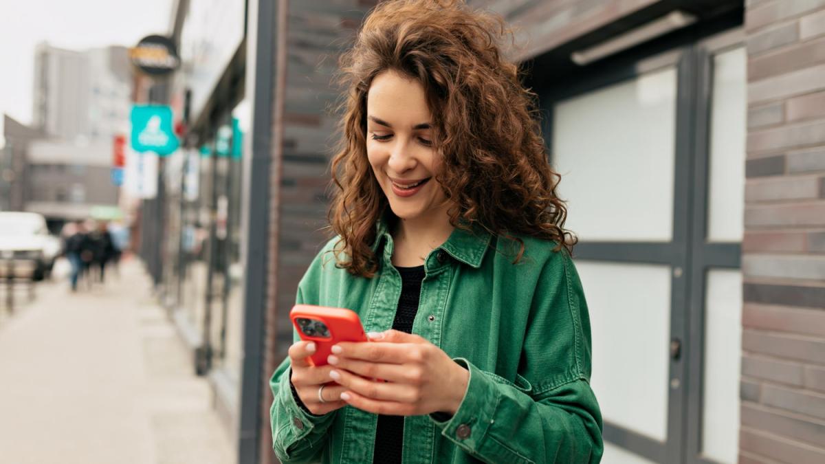 Кудрявая девушка в зелёной рубашке с телефоном