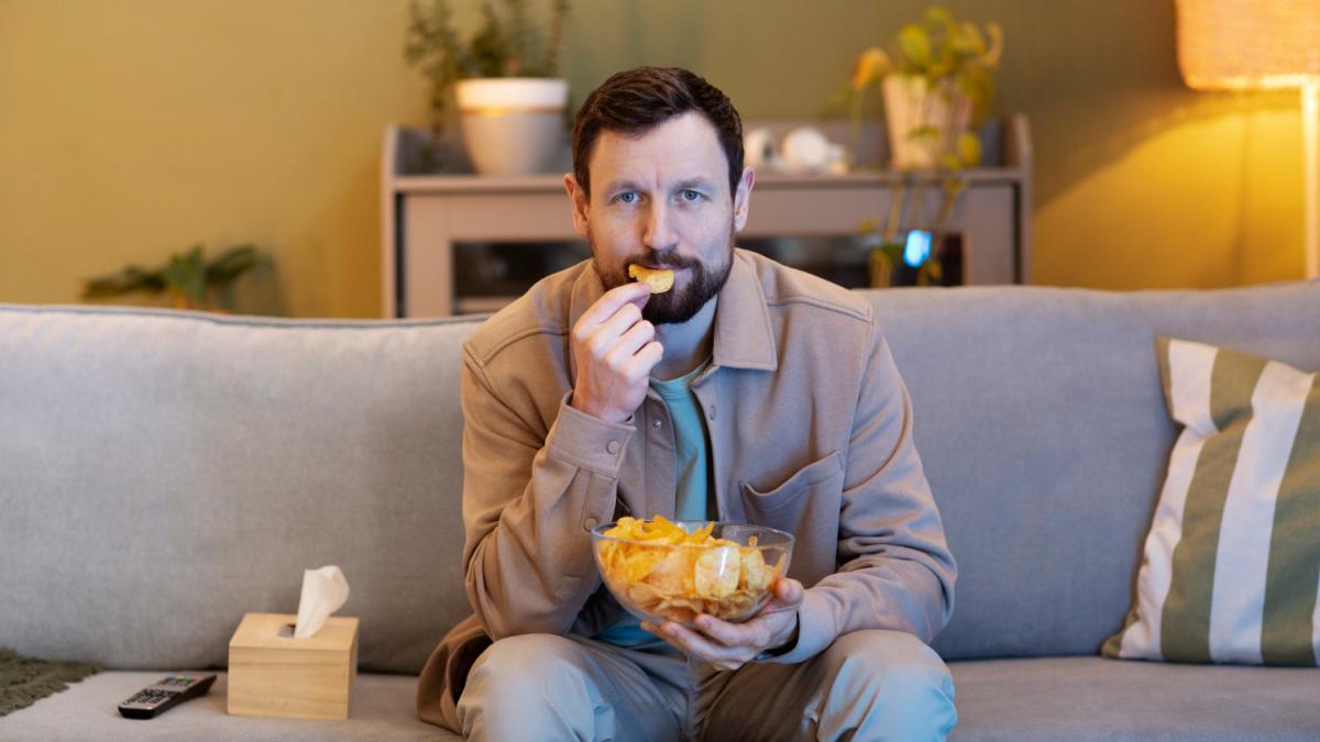 Человек смотрит телевизор и ест чипсы