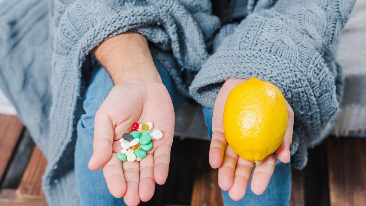 Женщина в свитере держит в руках лимон и аптечные витамины