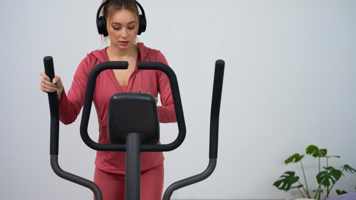 Девушка в наушниках занимается на эллипсе